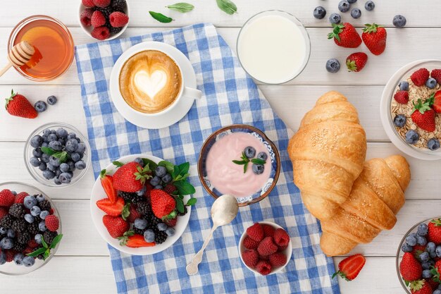 Petit déjeuner continental copieux. Croissants français croustillants, muesli, verre de lait frais, tasse de café noir chaud et beaucoup de baies sucrées pour de savoureux repas du matin. Délicieux début de journée, vue de dessus