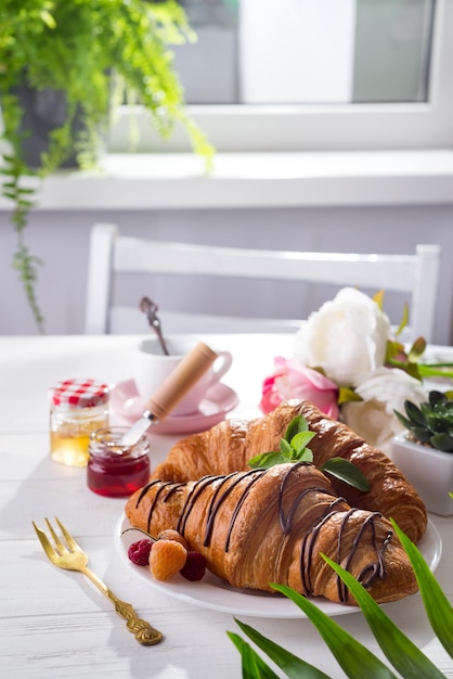 Petit déjeuner continental croissant fraîchement sorti du four, décoré avec de la confiture et du chocolat