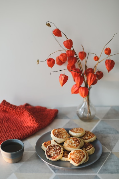 petit-déjeuner avec des crêpes au fromage cottage maison, une tasse de thé et des fleurs dans un vase sur la table