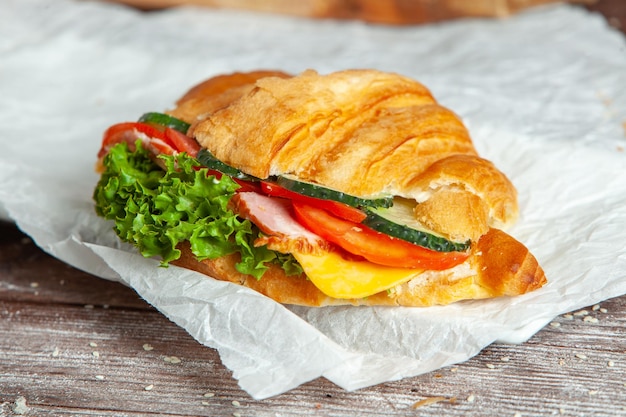 Petit-déjeuner de croissant frais avec jambon fromage et feuille de salade sur fond de bois blanc