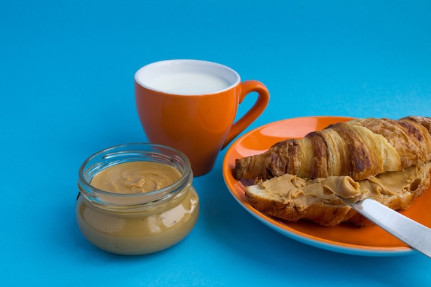 Petit déjeuner: croissant avec pâte d'arachide et lait sur le fond bleu