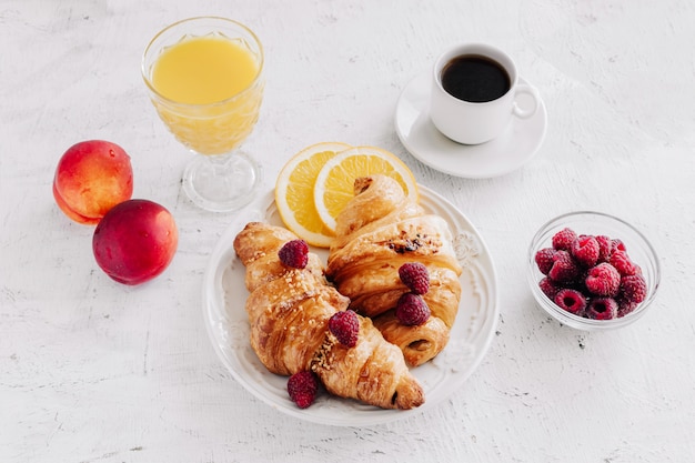 Petit déjeuner avec croissants, une tasse de café, framboises et jus d'orange vue de dessus