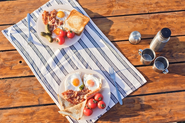 Petit-déjeuner dans la nature eggsufs au plat avec du pain grillé au bacon et du café chaud dans un thermos