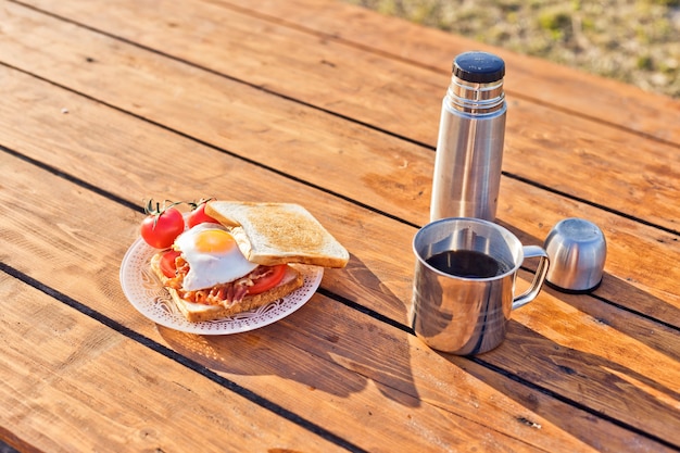 Petit-déjeuner dans la nature eggsufs au plat avec du pain grillé au bacon et du café chaud dans un thermos