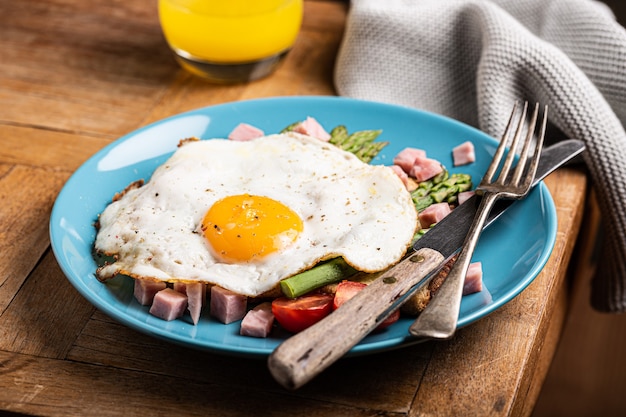 Petit-déjeuner ou déjeuner sain avec oeuf au plat, pain grillé, asperges vertes et tomates sur plaque bleue sur la vieille table en bois