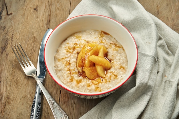 Un petit déjeuner délicieux et sain - gruau au lait avec des bananes, des noix et des fruits confits dans un bol blanc sur une table en bois. Petit-déjeuner sain