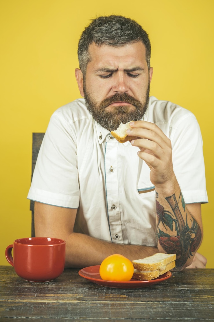 Photo petit-déjeuner du matin concept de nourriture de loisirs homme affligé en chemise blanche assis au bureau en train de manger du pain grillé sur