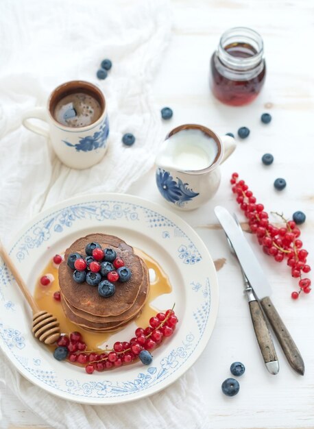 Petit déjeuner ensemble crêpes de sarrasin avec crème sure au miel de baies fraîches et tasse de café sur fond de bois blanc