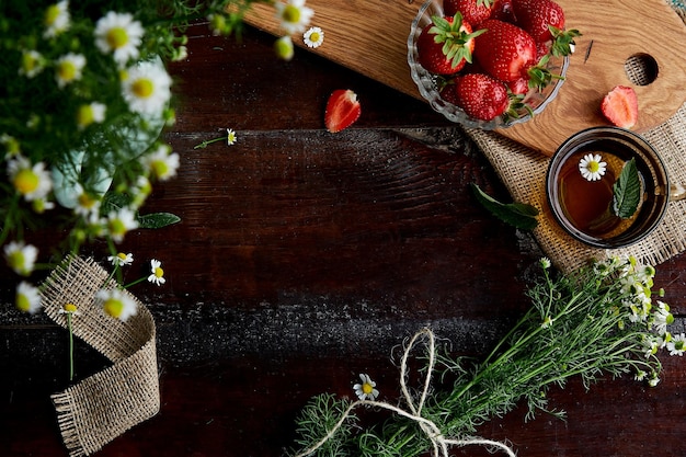 Petit déjeuner d'été naturel Fraises fraîches fleurs de camomille thé bio et menthe sur table en bois Mode de vie estival esthétique Belle nourriture Se connecter avec la nature Espace de copie