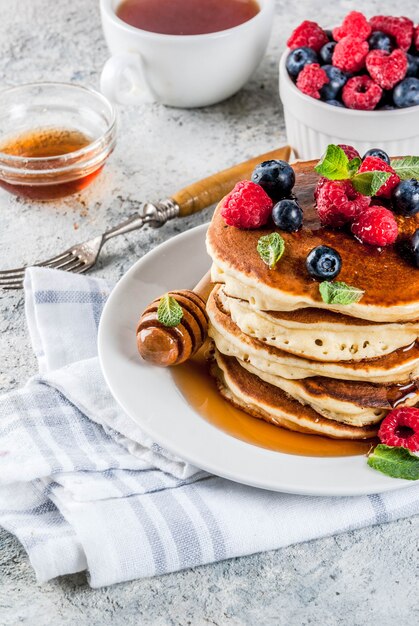 Petit-déjeuner d'été sain, crêpes américaines classiques faites maison avec des baies fraîches et du miel, surface de pierre gris clair du matin