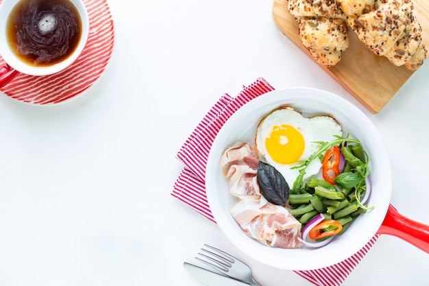 Petit-déjeuner européen: œuf en forme de cœur, bacon, haricots verts sur une table blanche. Mise au point sélective. Vue d'en-haut. Copiez l'espace.