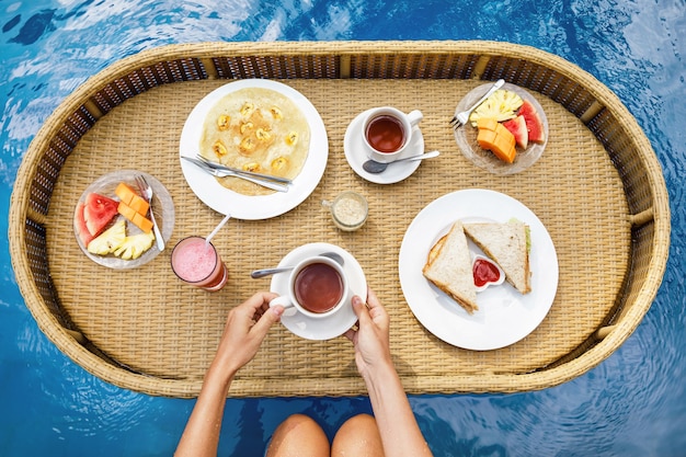 Petit déjeuner flottant dans la piscine. Plateau de paille avec des aliments différents.