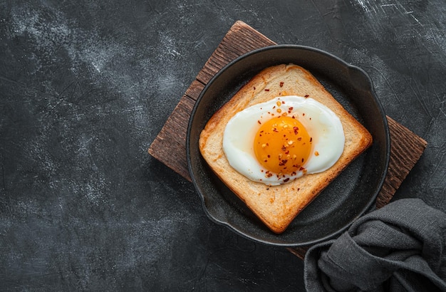 Petit-déjeuner frais avec des œufs au plat dans une poêle à frire sur fond sombre. Œufs frits sur toast frit. Vue de dessus, copiez l'espace.