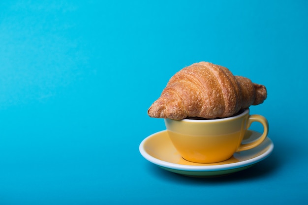 Petit déjeuner français. belle tasse de café jaune cappuccino avec croissant sur fond bleu