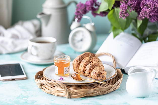 Petit déjeuner français croissant, confiture, tasse de café, lait et crème et fleurs lilas.