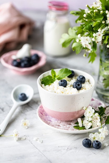 Petit-déjeuner fromage cottage aux bleuets, crème, lait sur un tableau blanc et une branche de fleurs.