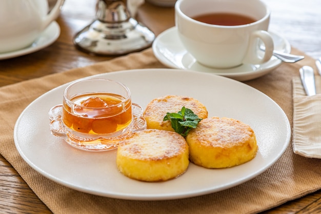 Petit-déjeuner avec des gâteaux au fromage avec de la confiture. En arrière-plan une tasse de thé.