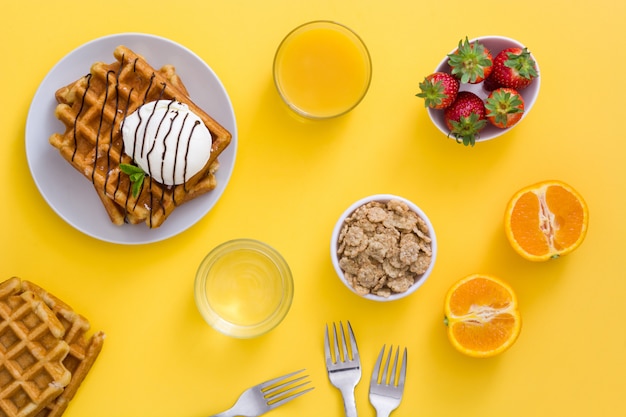 Petit déjeuner gaufre avec jus de crème glacée, fruits et céréales sur tableau jaune