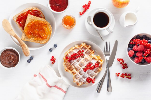 Petit déjeuner avec gaufre, pain grillé, baies, confiture, pâte à tartiner au chocolat et café. Vue de dessus