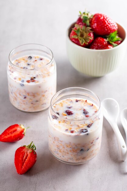 Petit-déjeuner granola dans des bocaux en verre avec du yaourt ou du lait sur fond de ciment gris. Alimentation saine