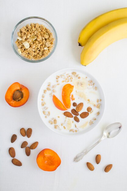 Petit-déjeuner granola avec des fruits au lait et des amandes dans le bol blanc sur la nappe blanche Vue de dessus Gros plan Emplacement vertical