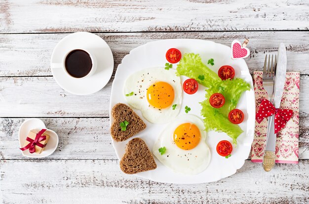 Petit déjeuner le jour de la Saint-Valentin - œufs frits et pain en forme de cœur et légumes frais. Vue de dessus