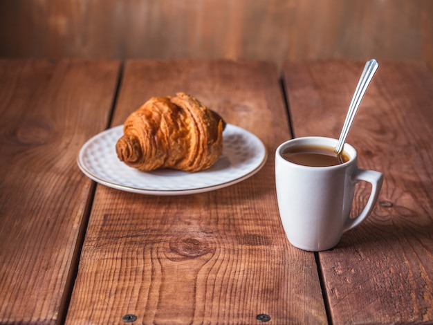 Petit-déjeuner Léger Avec Croissant Et Café Noir Dans Une Tasse Blanche Avec Une Cuillère Sur La Table