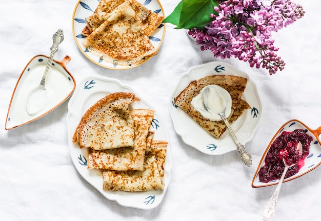 Petit-déjeuner maison confortable sur fond clair crêpes de grains entiers confiture de canneberges bouquet de lilas vue de dessus