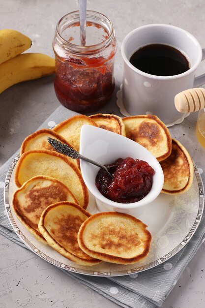 Petit-déjeuner maison: crêpes avec de la confiture, du miel, des bananes et une tasse de café sur une serviette grise sur fond de béton