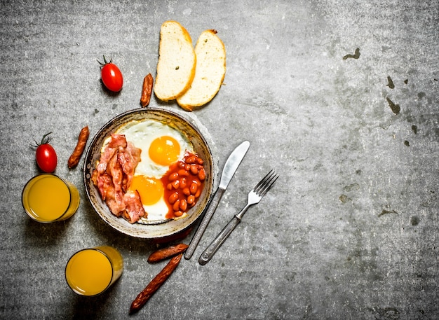 Petit déjeuner le matin. Bacon, œufs au plat avec haricots et jus d'orange. Sur la table en pierre.