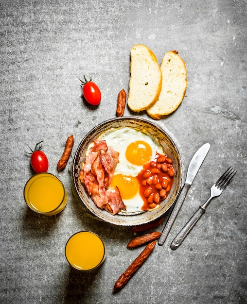 Photo petit déjeuner le matin. bacon, œufs au plat avec haricots et jus d'orange. sur la table en pierre.