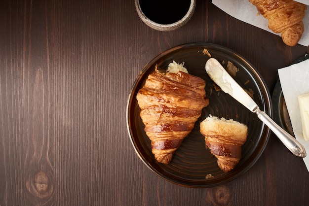 Petit déjeuner le matin avec croissant et tranche sur assiette, tasse de café, confiture et beurre.