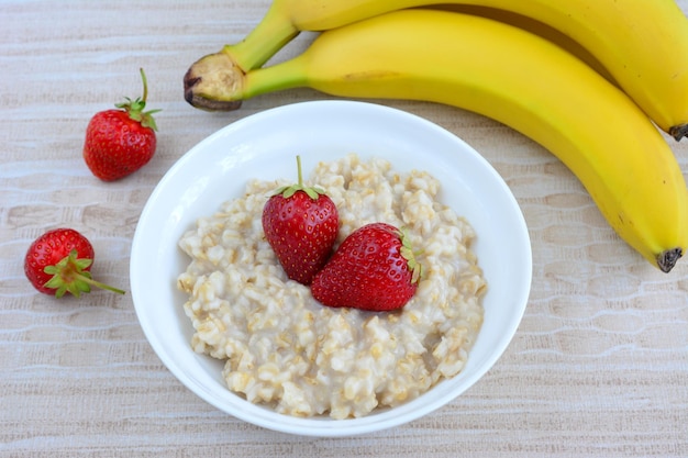 petit-déjeuner matinal avec bouillie, banane et fraises sur fond beige, gros plan