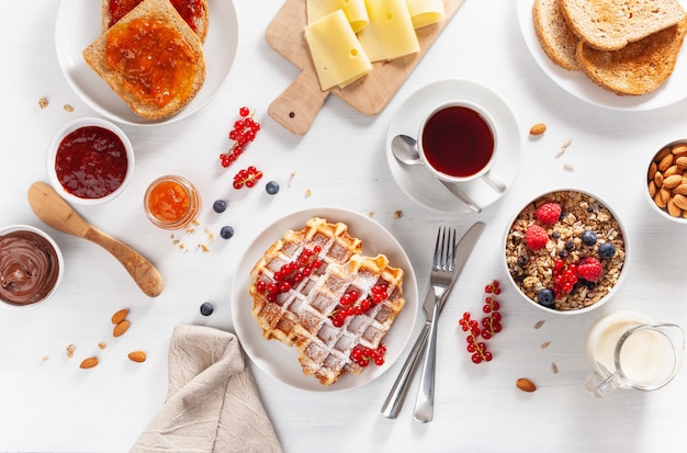 Petit déjeuner avec noix de céréales, gaufre, pain grillé, confiture, tartinade au chocolat et café. Vue de dessus