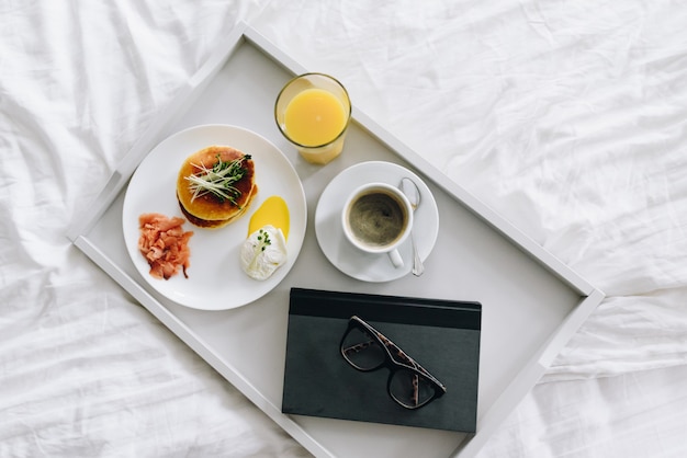 Petit-déjeuner nutritif et savoureux avec du café au lit sur un plateau avec des lunettes et livre vue de dessus