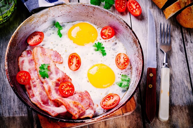 Petit-déjeuner avec œufs frits bacon tomates et persil sur table rustique