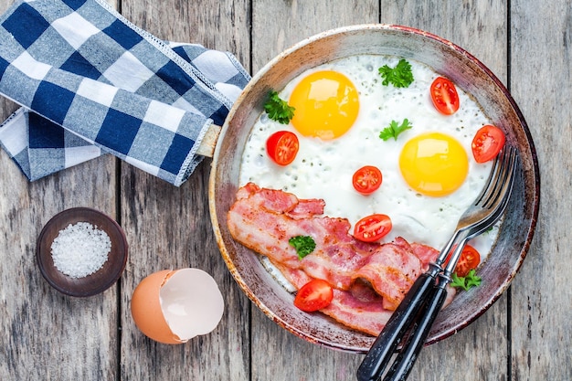 Petit-déjeuner avec œufs frits bacon tomates et persil sur table rustique