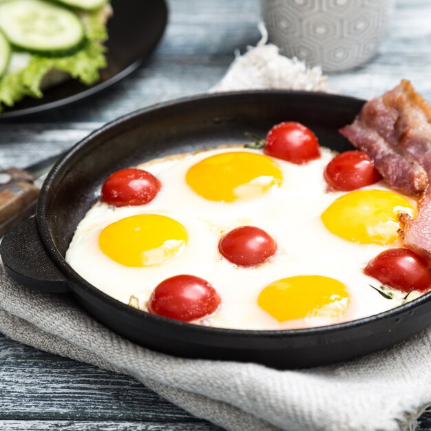 Petit-déjeuner avec des œufs, des tomates cerises, du bacon et des toasts grillés