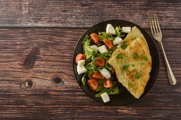Petit déjeuner - omelette aux œufs avec tomates cerises, mozzarella et vert. Table en bois avec espace de copie.