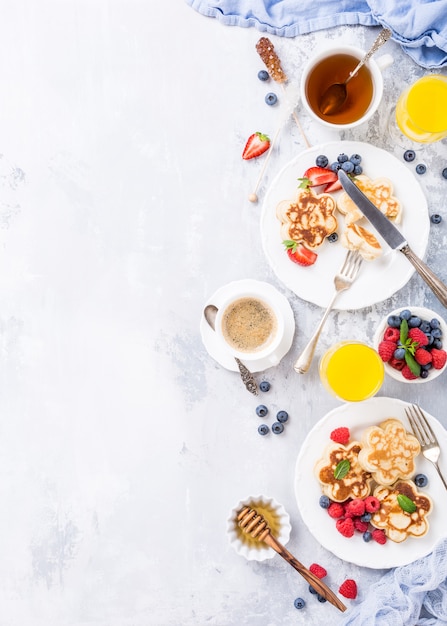 Photo petit-déjeuner avec des pancakes écossais sous forme de fleurs, des baies et du miel sur une table en bois clair