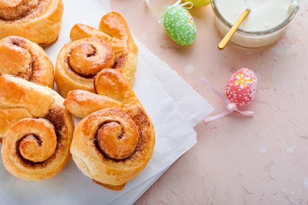 Petit-déjeuner de Pâques Holliday concept Petits pains de lapin de Pâques à la cannelle à base de pâte à levure avec glaçage orange décorations de Pâques oeufs colorés sur fond de printemps rose Carte de vacances de Pâques