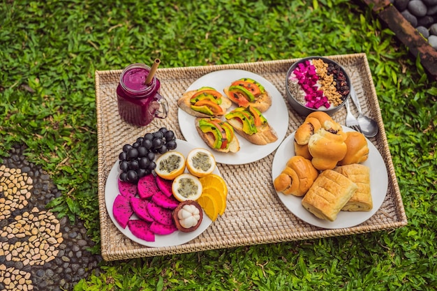 Petit-déjeuner sur un plateau avec des petits pains aux fruits sandwichs à l'avocat bol de smoothie debout sur l'herbe