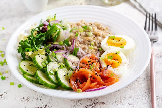 Petit-déjeuner porridge d'avoine avec des œufs bouillis, du saumon salé, du concombre et des oignons rouges Nourriture saine et équilibrée Nourriture à la mode