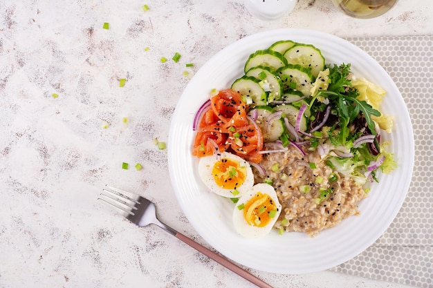 Petit-déjeuner porridge d'avoine avec des œufs bouillis salé saumon concombre et oignons rouges nourriture saine équilibrée nourriture à la mode vue supérieure à plat