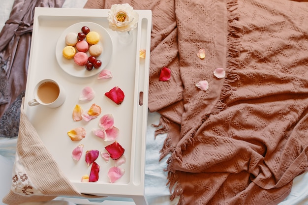 Petit-déjeuner romantique au lit avec soucoupe de pétales de rose avec macarons et cerises