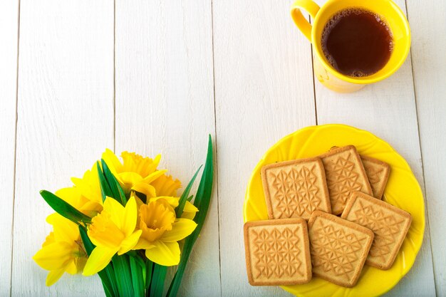 Petit déjeuner romantique. Jonquille près de thé et biscuits sur fond de bois blanc. Vue de dessus.