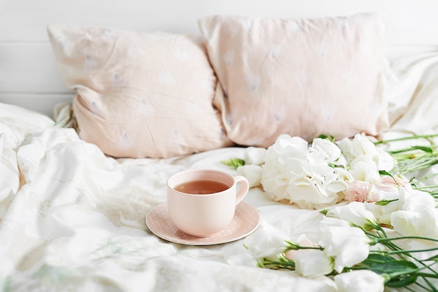 Petit-déjeuner romantique de la Saint-Valentin au lit avec tasse de thé et fleurs sur le lit
