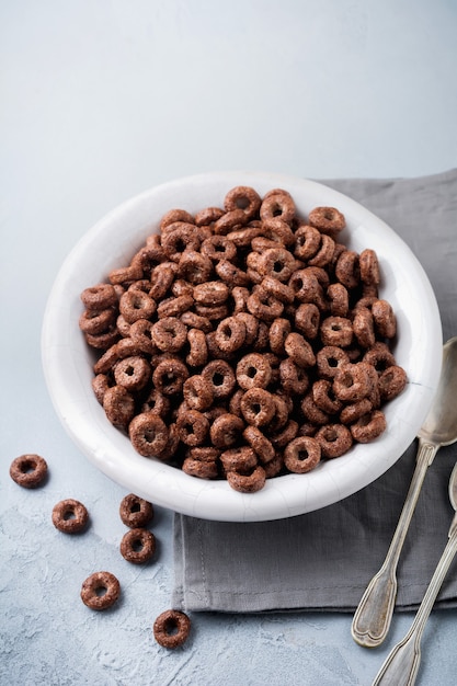 Petit-déjeuner sain avec des anneaux de maïs au chocolat, des baies de groseille rouge, du yogourt et du thé sur un fond de béton gris