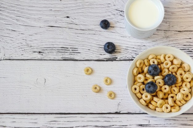 Petit-déjeuner sain Anneaux de miel avec myrtilles et lait dans un bol sur le fond en bois de la table