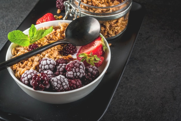 Petit-déjeuner sain. Baies et fruits d'été. Yaourt grec fait maison avec granola, mûres, fraises et menthe. table en pierre noire, avec les ingrédients.